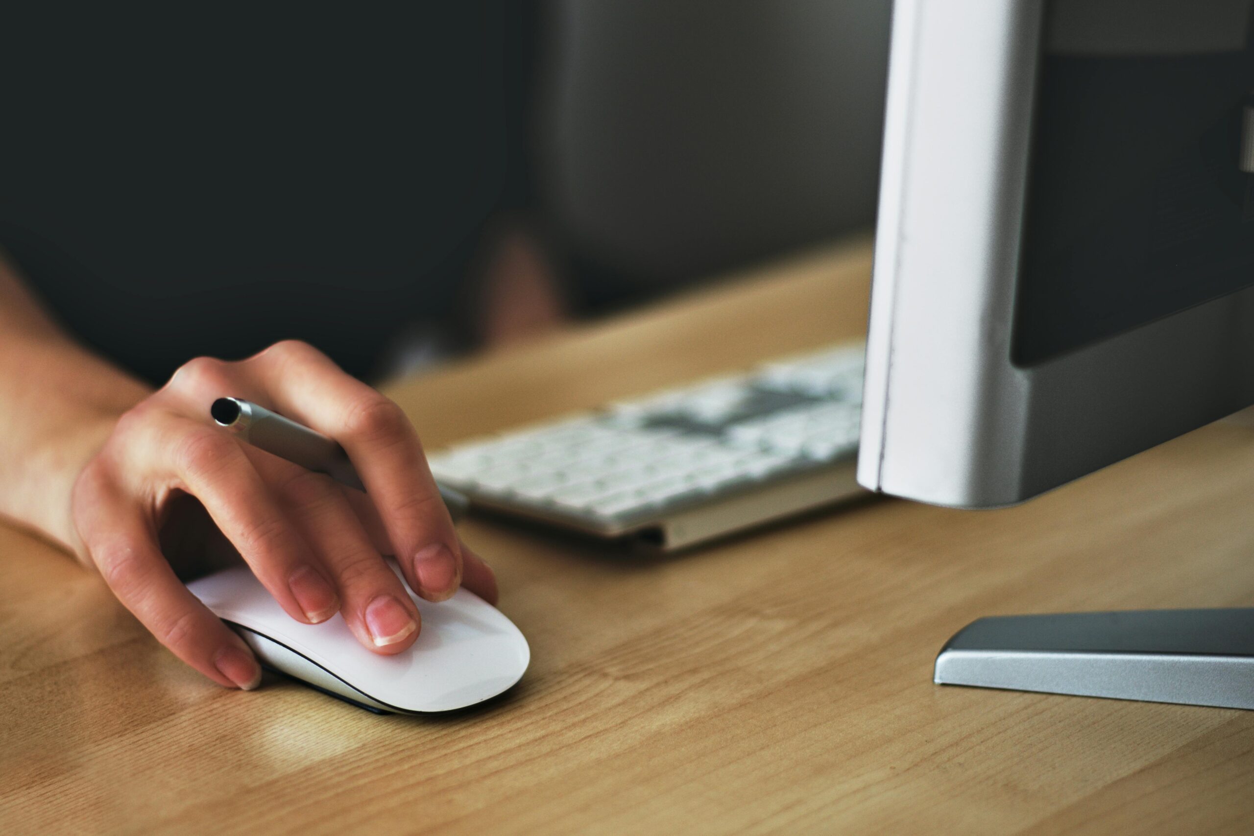 Picture of a close up of a desk with a person holding a pen with the hand on a mouse